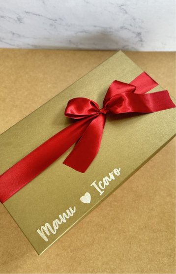 Caixa dourada com laço vermelho e nomes do casal na tampa